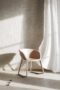 Der Riseup Stuhl in einer atmosphärischen Darstellung. Auf der rechten Seite wird eine Gardine durch das offene Fenster in Bewegung gesetzt und an der Wand hinter dem Stuhl zeichnet sich stark die Sonne ab.