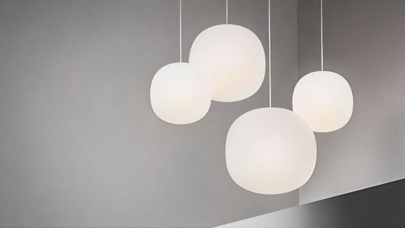 Vier große Glasleuchten hängen in einem Raum mit grauen Wänden.