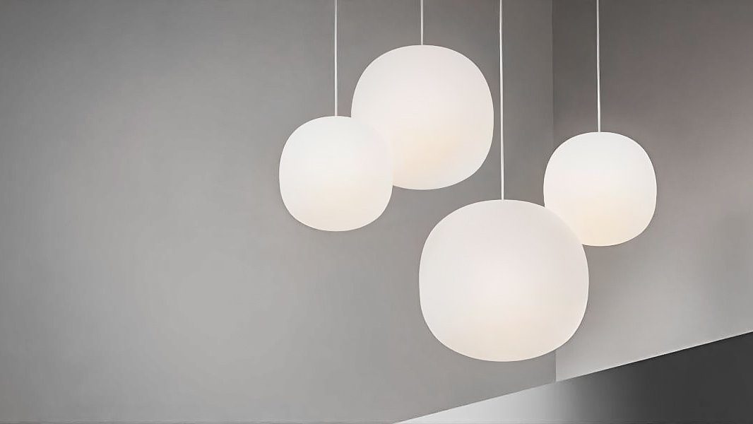 Vier große Glasleuchten hängen in einem Raum mit grauen Wänden.